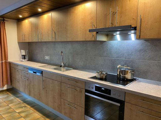 Moderne Küche mit Holzschränken, Edelstahlgeräten und Spüle in neutralen Farbtönen.