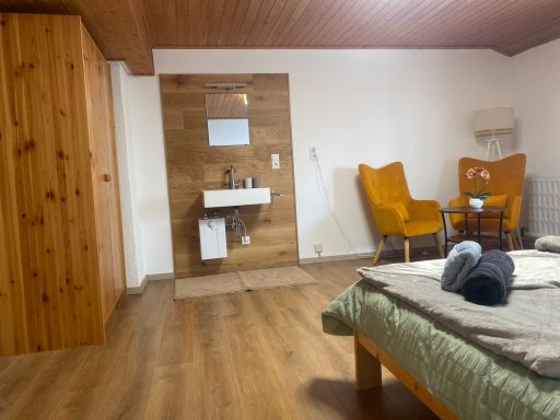 Gemütliches Zimmer mit Holzmöbeln, zwei Sessel und einem Badezimmerbereich.